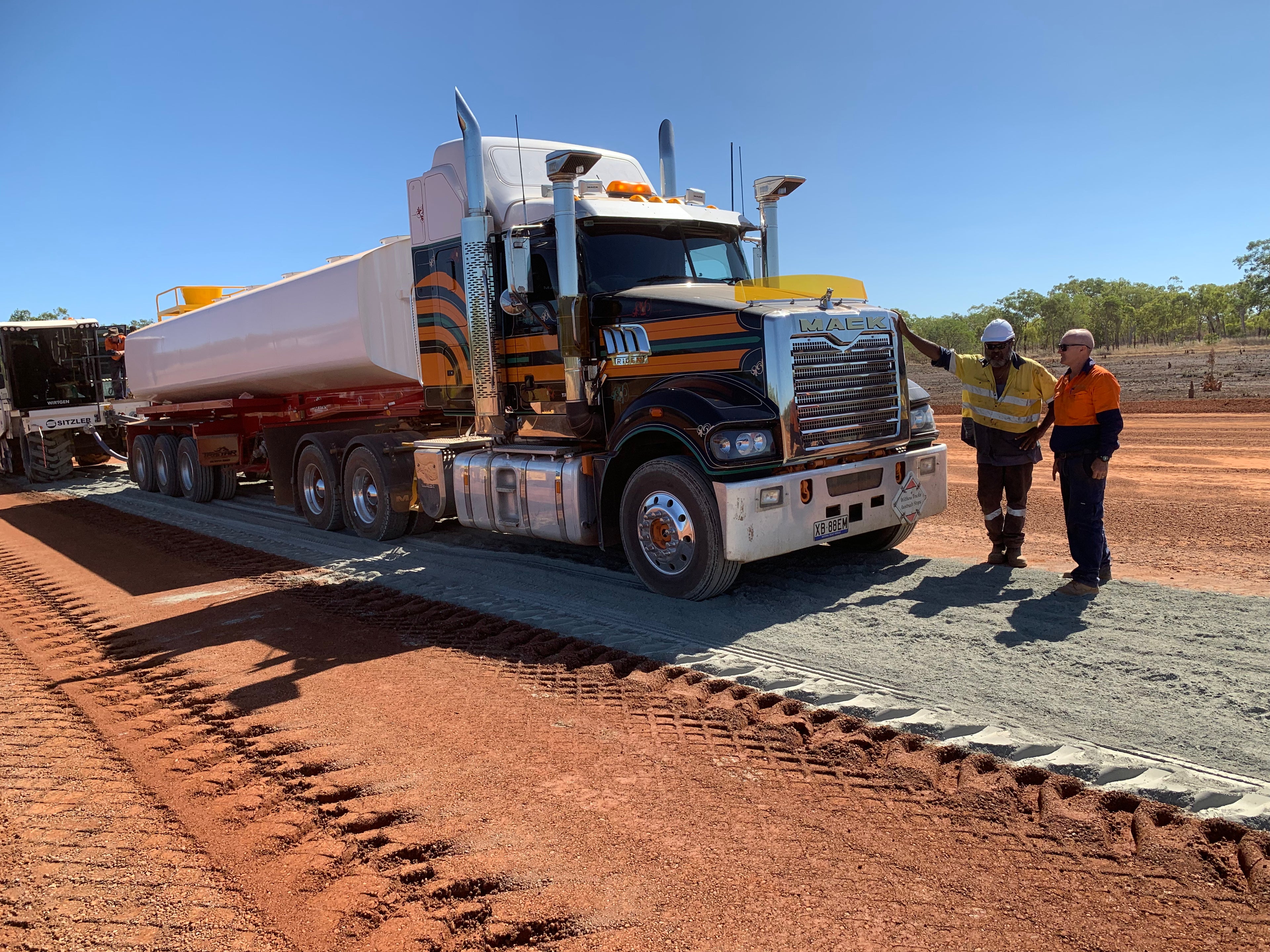 Large truck on a construction site with two workers in high-visibility clothing.