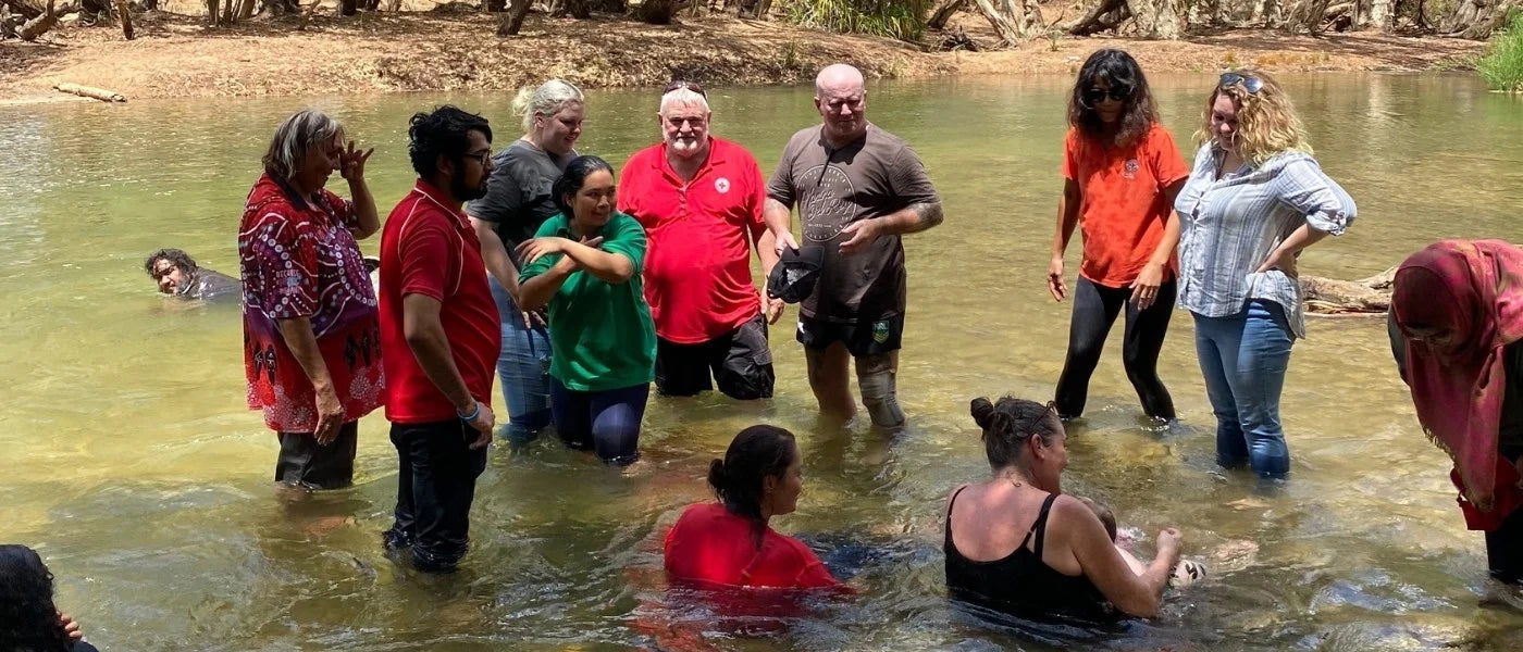 Group of people standing in shallow water of Katherine River during a Water Blessing ceremony